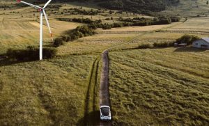 Ein Elektroauto fährt entlang eines Feldweges. Ebenfalls zu sehen ist ein Windrad. Wie gut ist jedoch die Klimabilanz von einem Elektroauto.